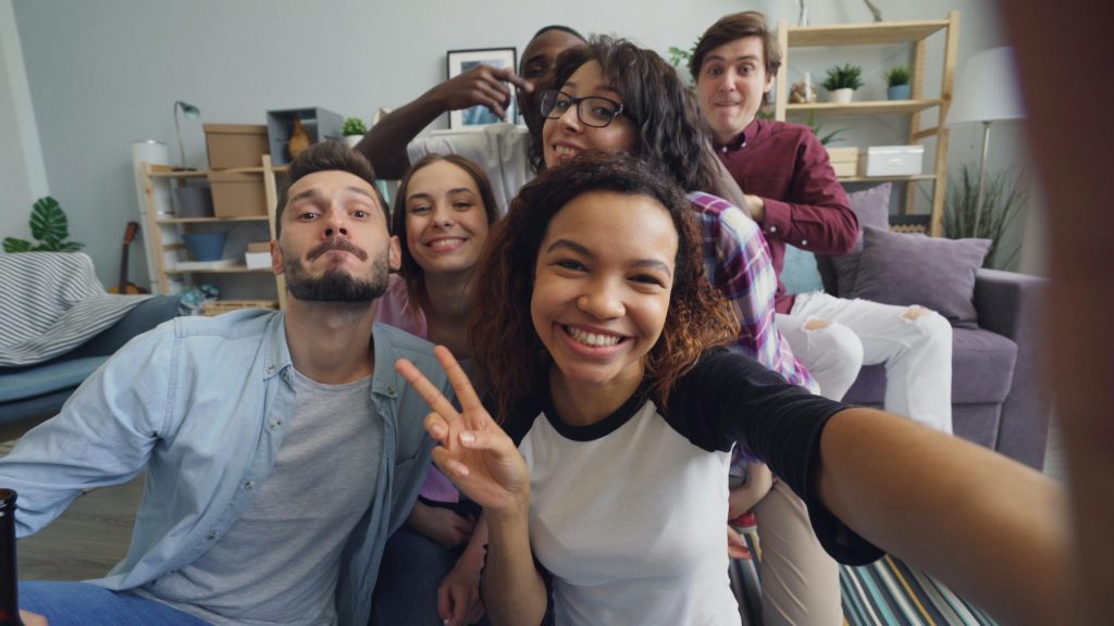 A diverse group of friends laughing and posing for a joyful indoor selfie.